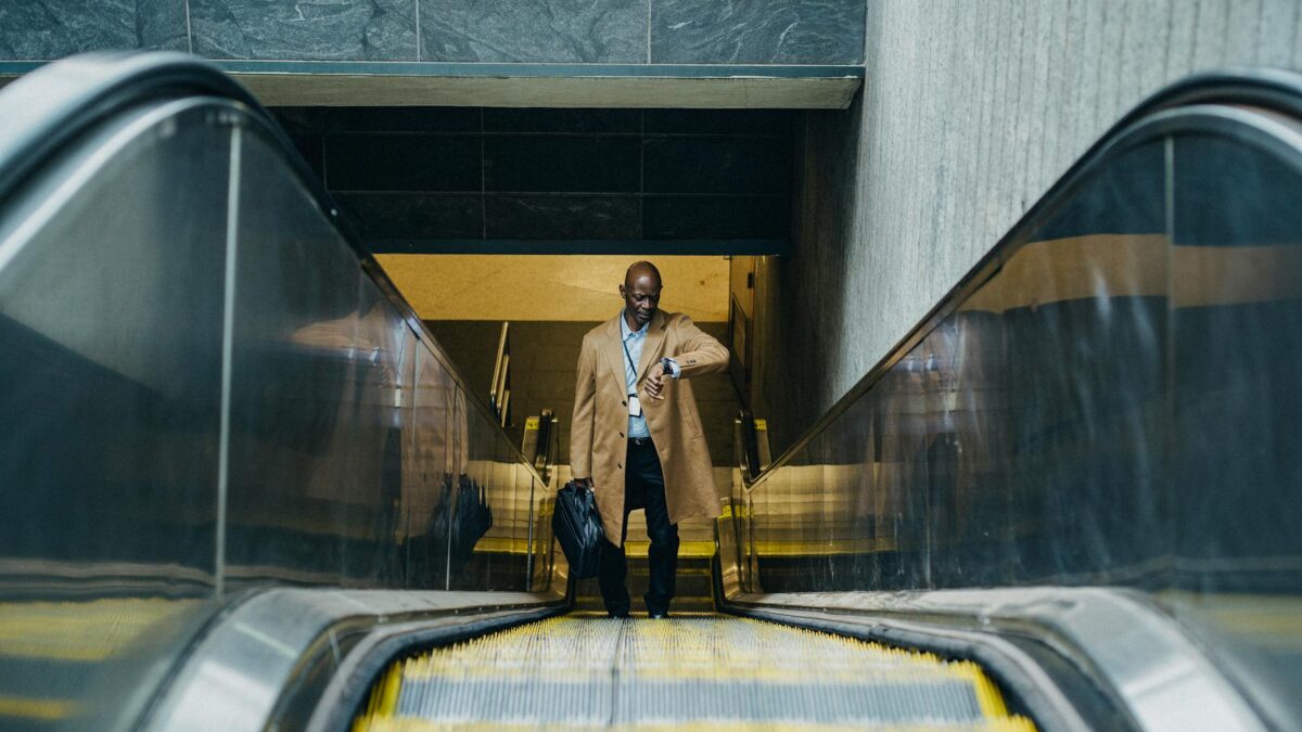 contemplative black businessman riding escalator and looking at wristwatch