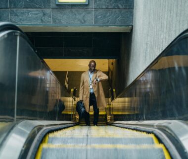 contemplative black businessman riding escalator and looking at wristwatch